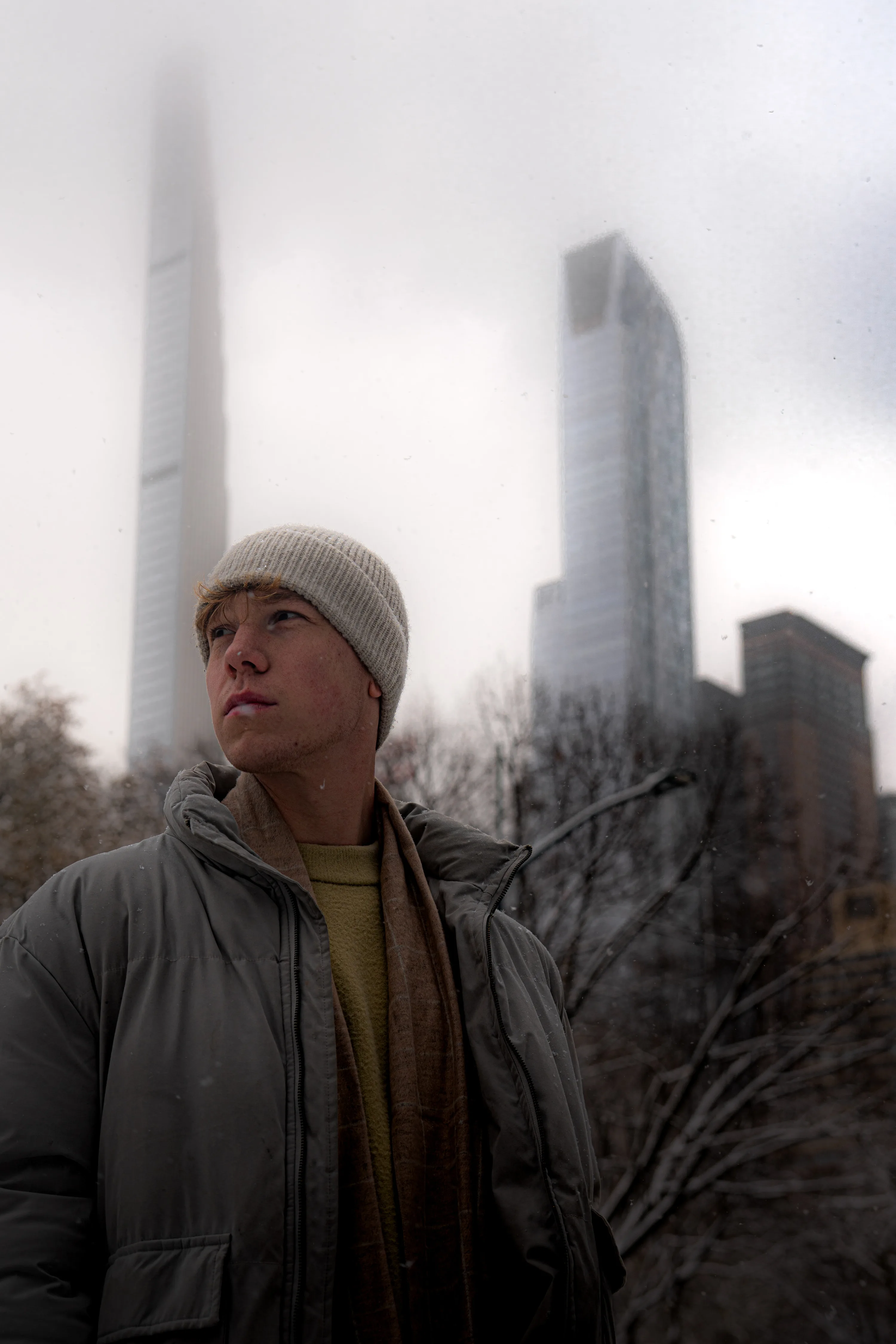 Henry Drösemeyer in a beanie and winter jacket, skyscrapers rising into fog behind him